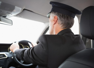 A suited chauffeur at the steering of a vehicle